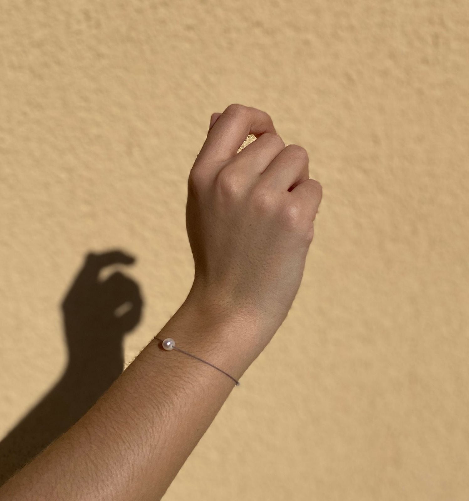 Bracelet perle porté au poignet devant un mur ocre
